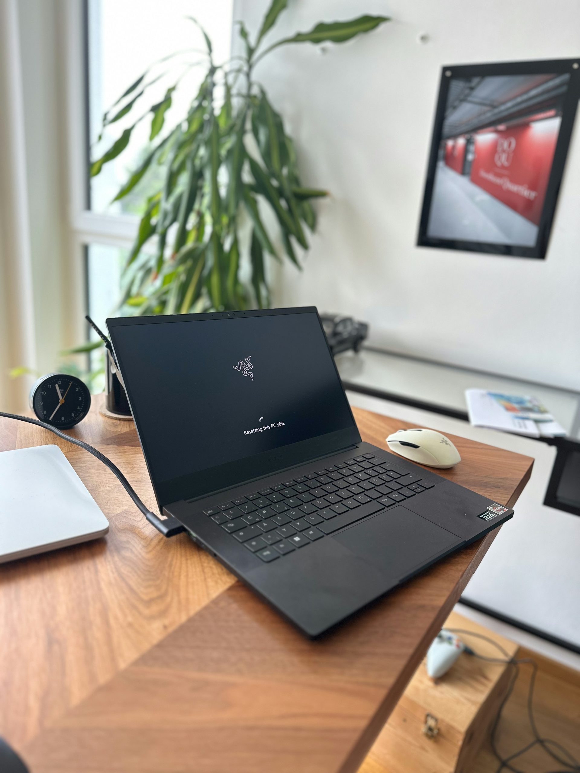 Ordinateur portable noir ouvert sur un bureau en bois avec une plante.