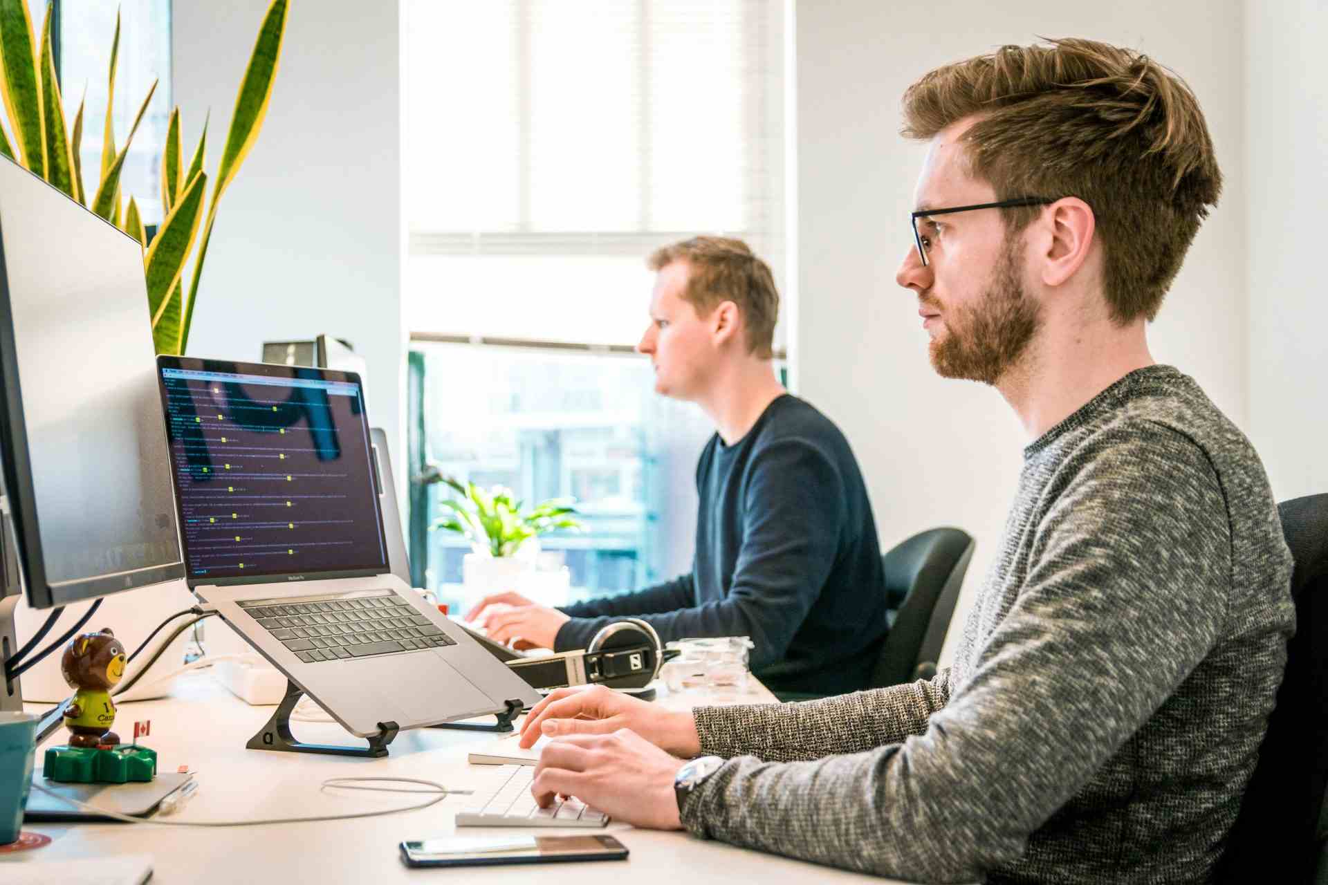 Un homme assis sur une chaise, portant un t-shirt gris à col rond et manches longues, utilise un clavier Apple Magic Keyboard.